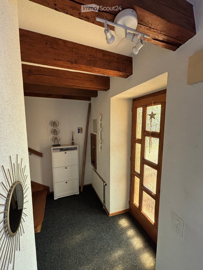 Carpeted hallway with wooden beams on the ceiling, a small cabinet with drawers, a mirror on the wall, and a door leading to another room.