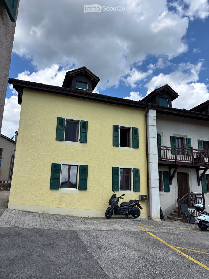 Two-story house with yellow walls, green shutters, and a balcony on the upper level. A scooter is parked in front of the house.