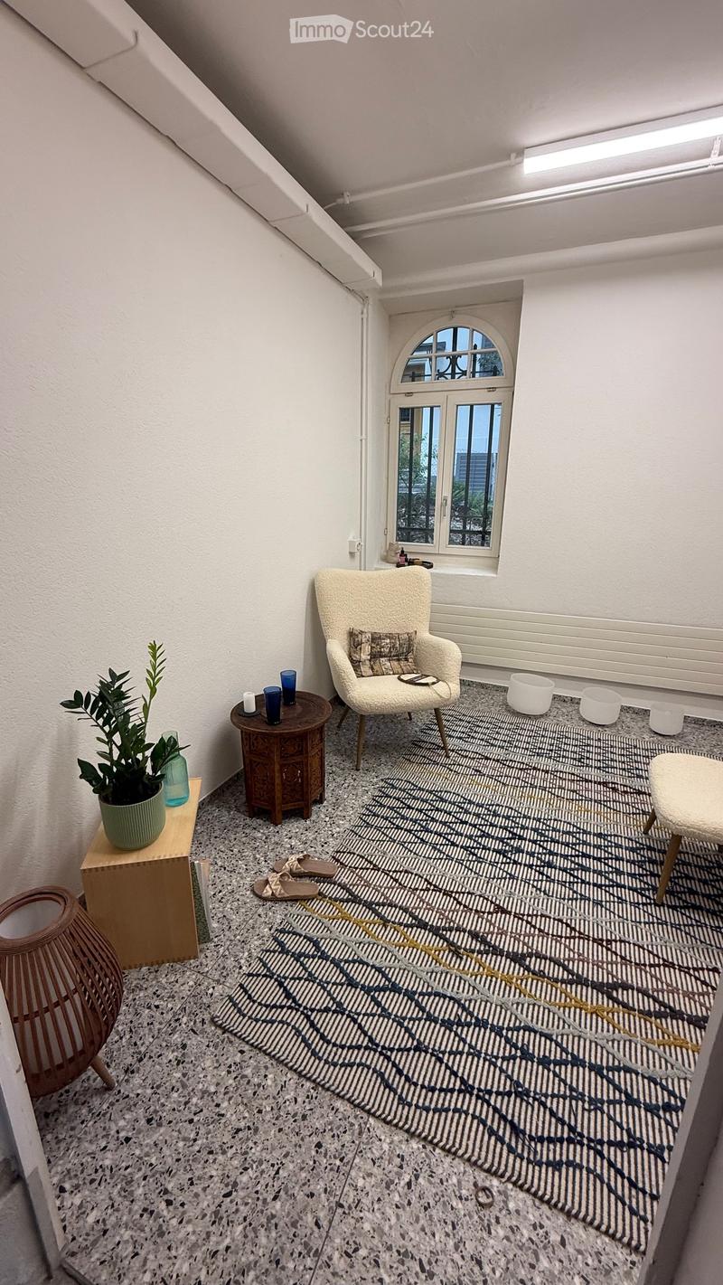 A modern, minimalist room with a white chair, small wooden table, plant, and decorative items on the floor.