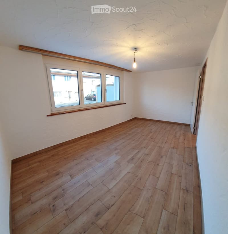 Empty room with wooden flooring, white walls, and a large window with wooden trim. The room has a simple, clean design with no furniture or decorations.