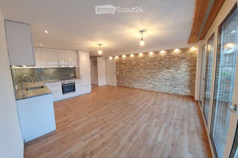 Modern kitchen with white cabinets, wooden flooring, and a stone accent wall. Features a sink, faucet, and oven.