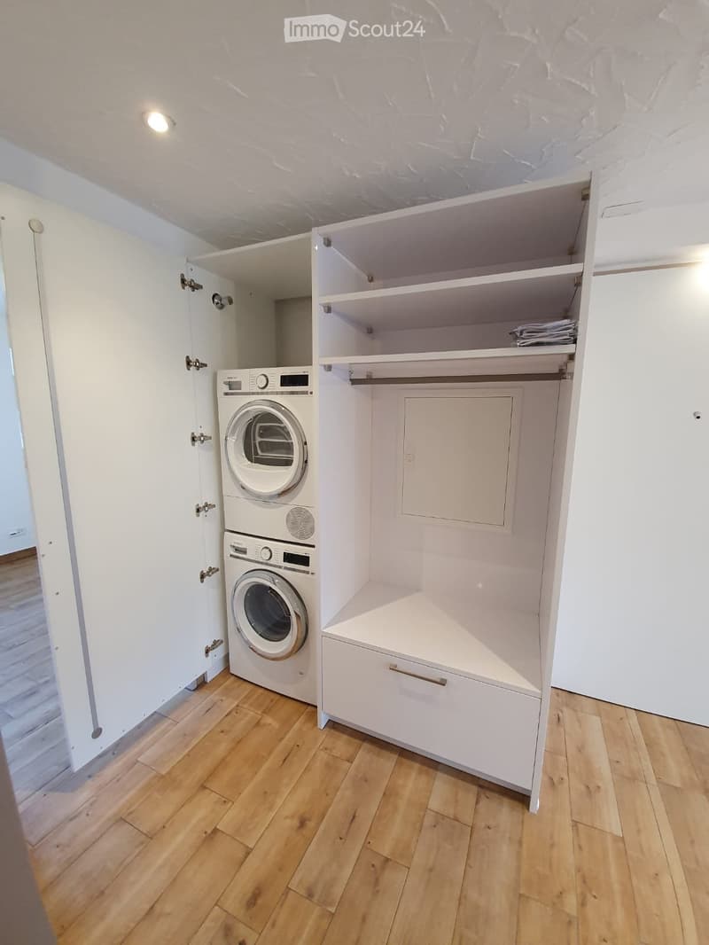A compact laundry room with a washing machine and dryer stacked vertically, white cabinets, and a wooden floor.