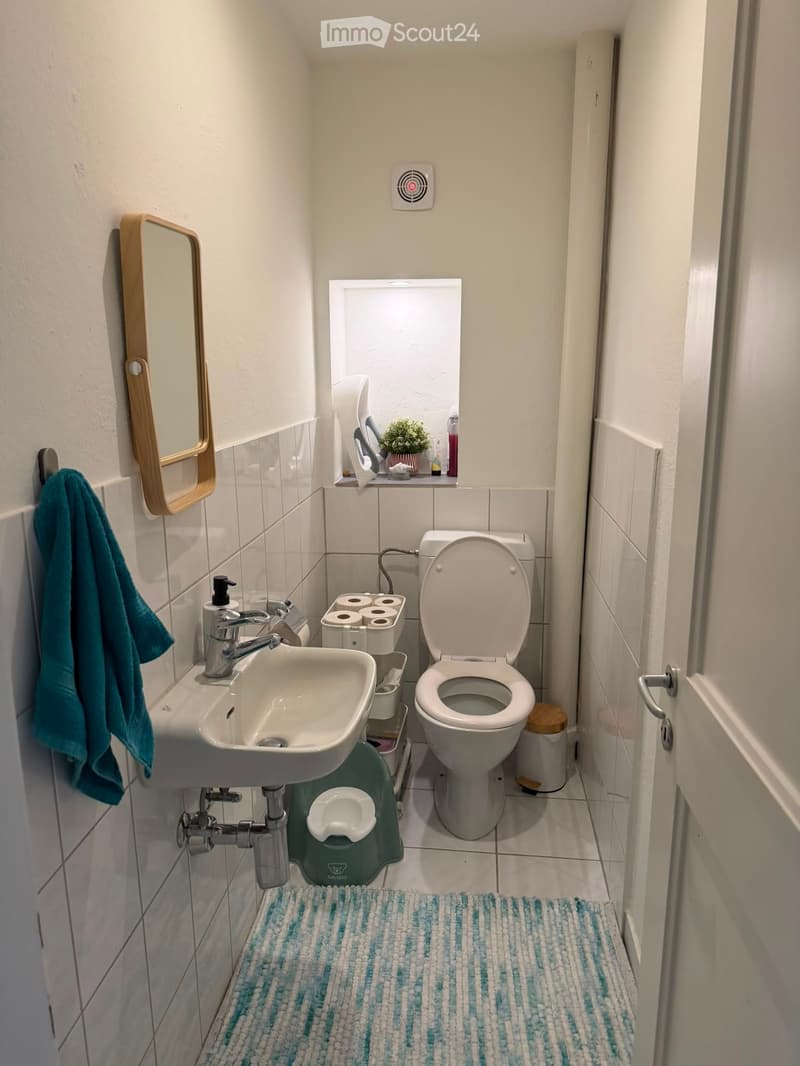 Compact bathroom with a toilet, sink, mirror, towel, toilet paper holder, small stool, and a blue and white striped rug.
