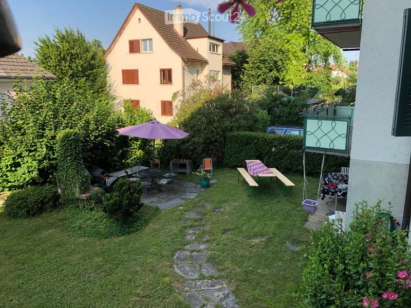 Garden with lawn, patio area, umbrella, tables, chairs, benches, and a small table with a pink tablecloth.