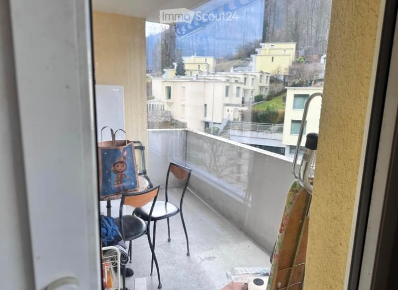 Balcony with a view of the city and surrounding buildings, featuring a small table, chairs, and a few personal items.