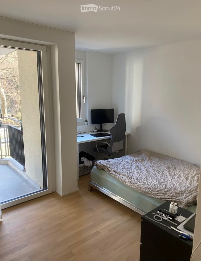 Cozy bedroom with a single bed, desk with a laptop, chair, and nightstand. Large window and balcony access.