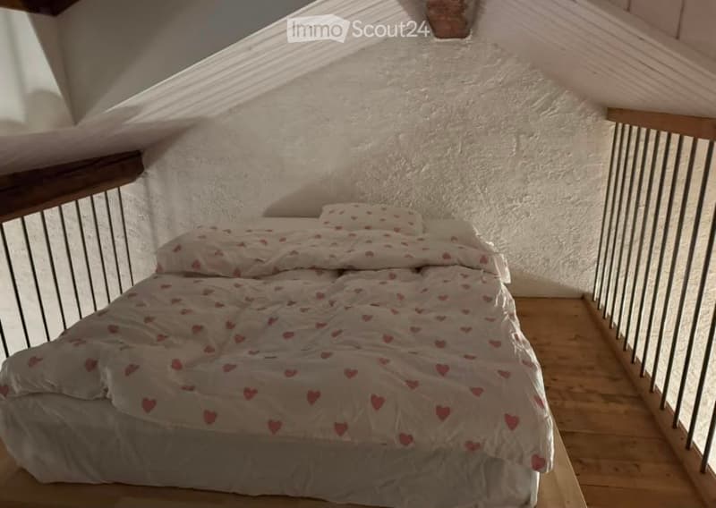 Cozy attic bedroom with wooden floors, slanted ceilings, and a bed with a heart-patterned blanket.