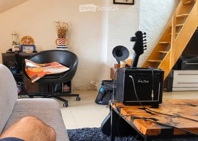 A modern living room with a grey sofa, black leather chair, wooden coffee table, guitar and amplifier, decorative vase, picture frame, and a small cabinet with drawers.