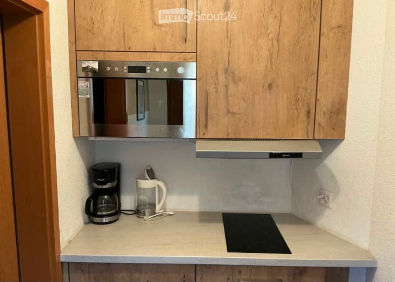Modern kitchen with light wood cabinets, stainless steel appliances, and a clean, minimalist design. Features include a coffee maker, electric kettle, and an induction cooktop on the countertop.