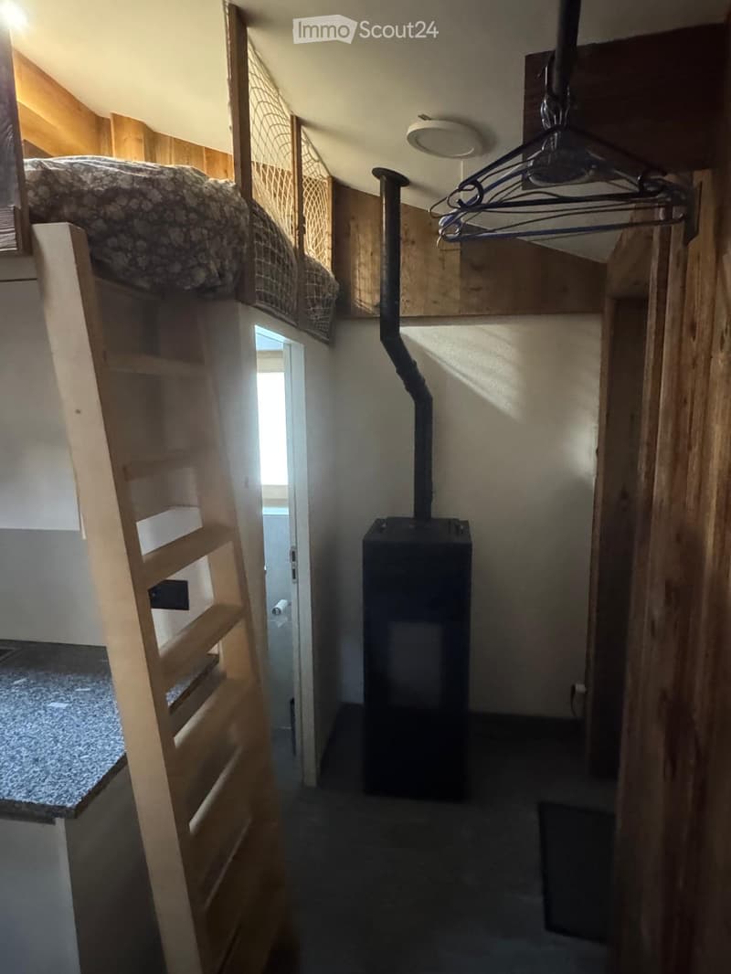 A narrow hallway with wooden walls, a staircase leading to a loft area, and a black heating unit in the center.