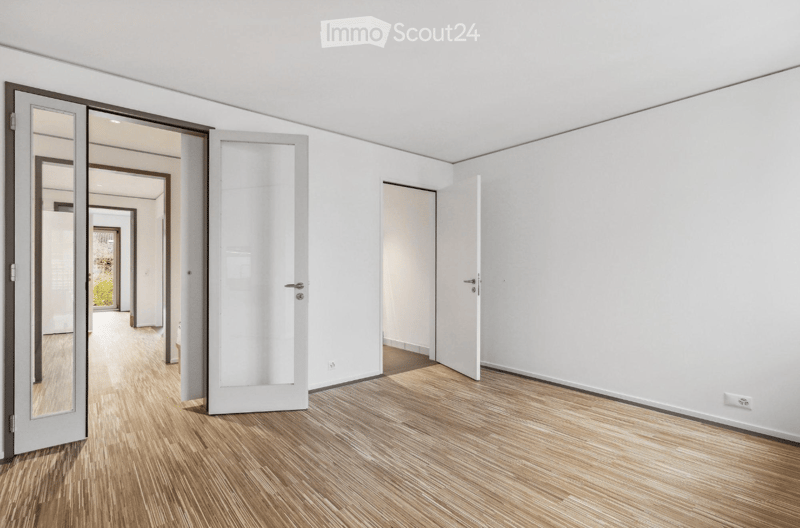Empty room with white walls, wooden flooring, and multiple doors leading to other spaces.