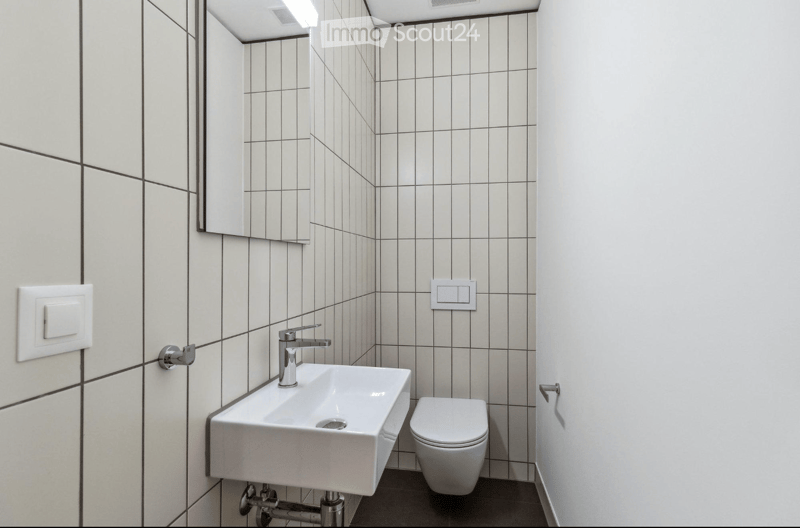 Modern bathroom with white tiles, a white sink with a chrome faucet, and a toilet. The walls are tiled with light gray tiles and black grout lines.