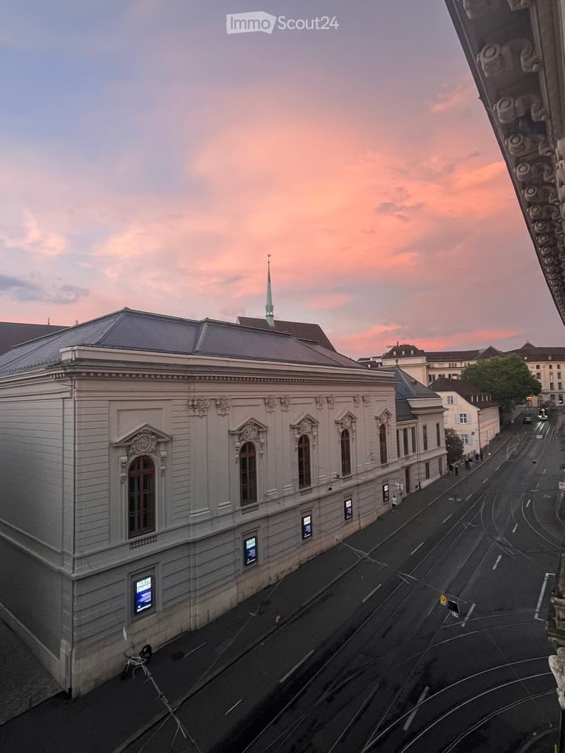 A large, classical-style building with ornate architectural details, multiple windows, and a steeply pitched roof, viewed from an elevated angle during sunset.