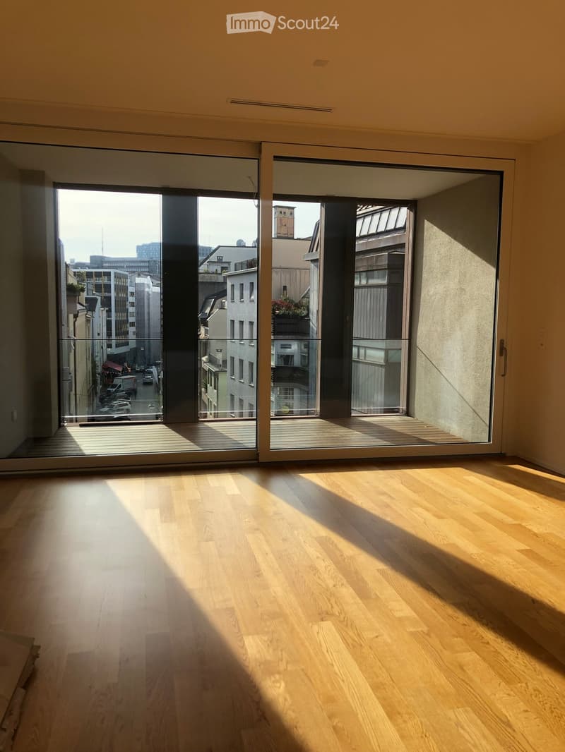 Empty room with light wooden flooring and large sliding glass doors leading to a balcony with city views.
