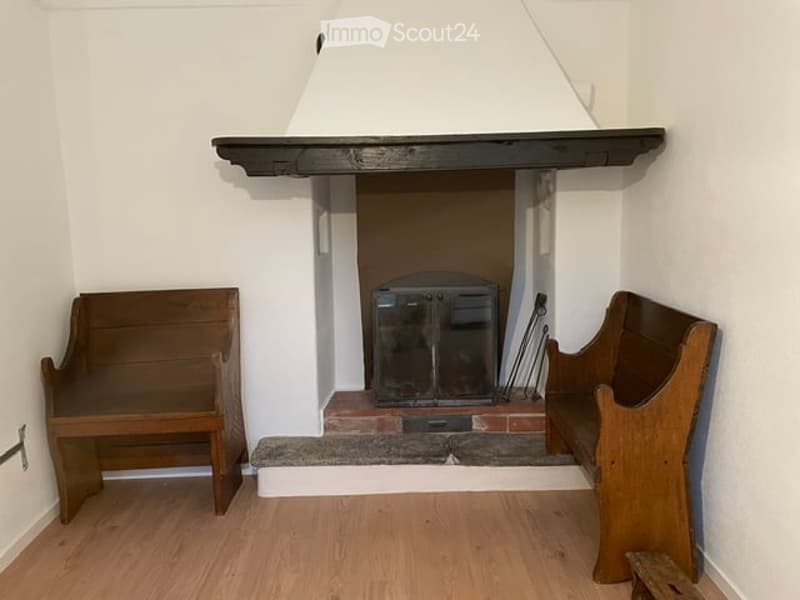 A small room with a fireplace, wooden benches on either side, and a wooden floor.