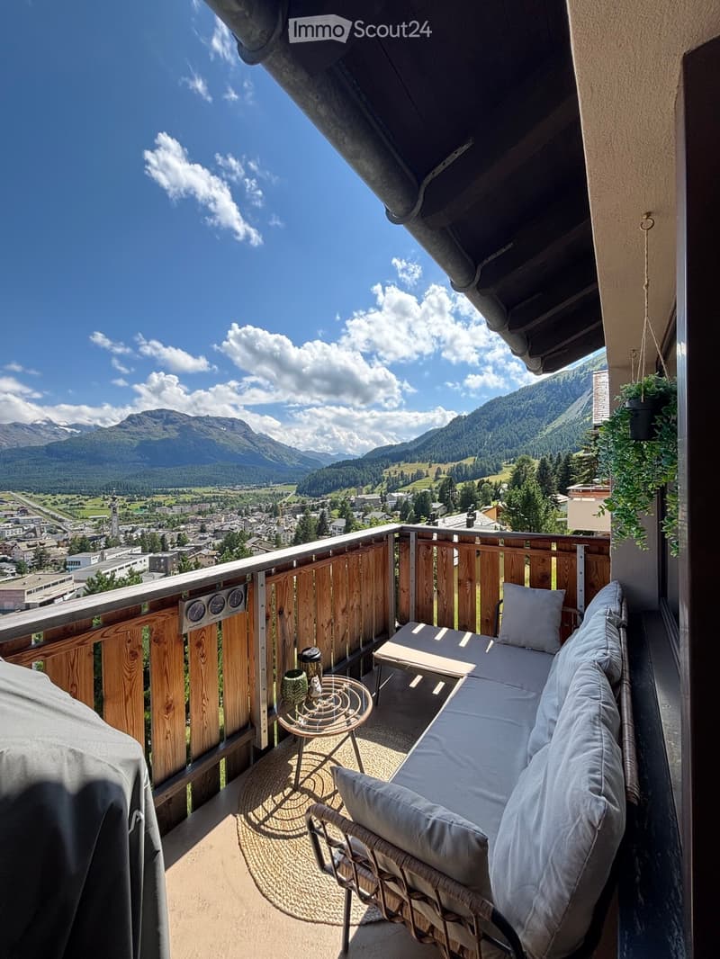 Balcony with wooden railing, sofa, small table, and scenic mountain view.