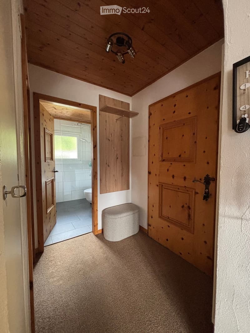 Carpeted hallway with wooden doors, a small wooden shelf, and a toilet visible through an open door.