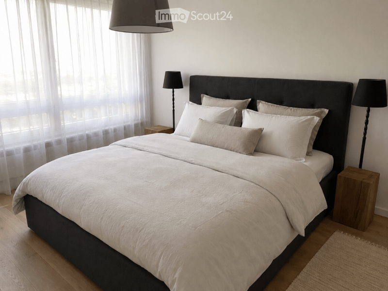 Modern bedroom with a large bed, multiple pillows, and a headboard. Wooden nightstands with lamps on either side, sheer curtains covering the windows, and a hanging pendant light above the bed.