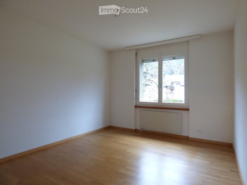 Empty room with wooden flooring, white walls, and a window with blinds. A radiator is visible below the window.