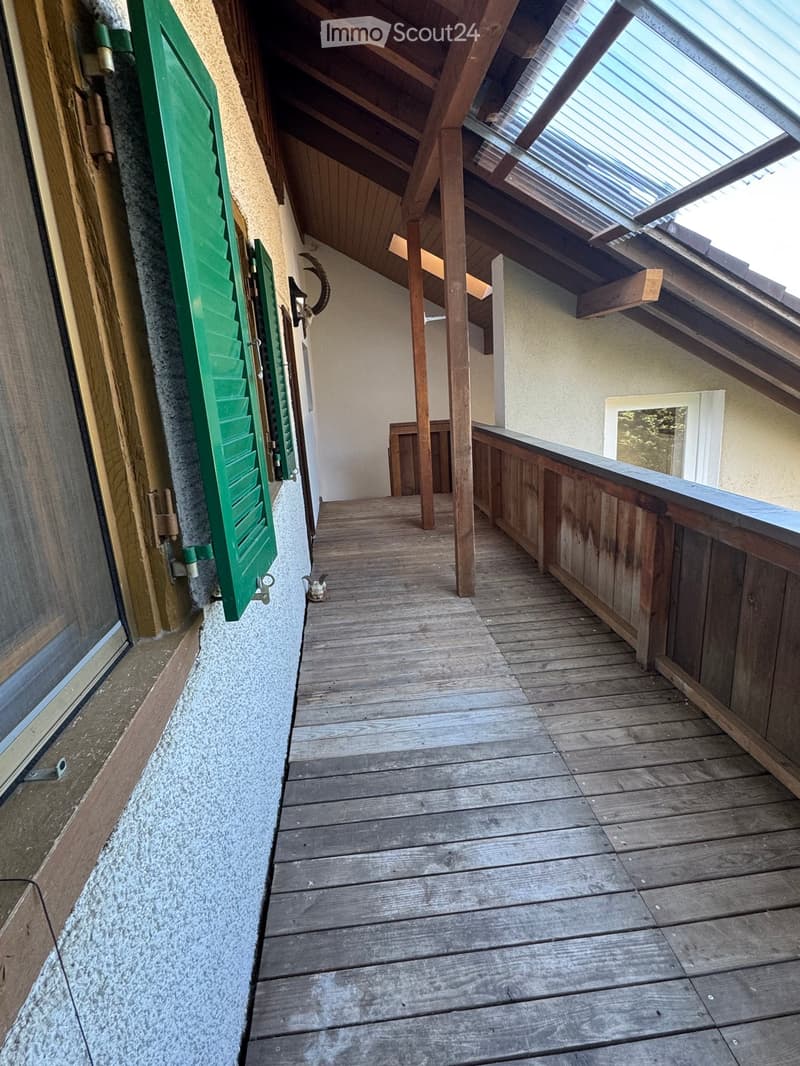 Wooden balcony with slanted wooden ceiling, green shutters, and a small window at the end.