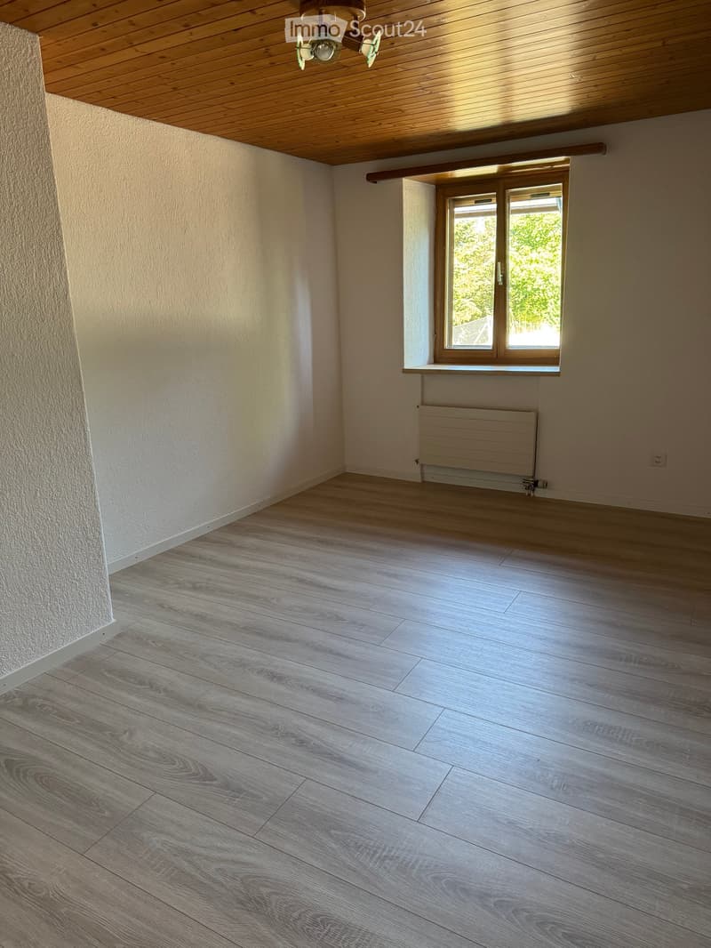 Empty room with wooden flooring, white walls, a window with wooden frame, and a radiator below the window.