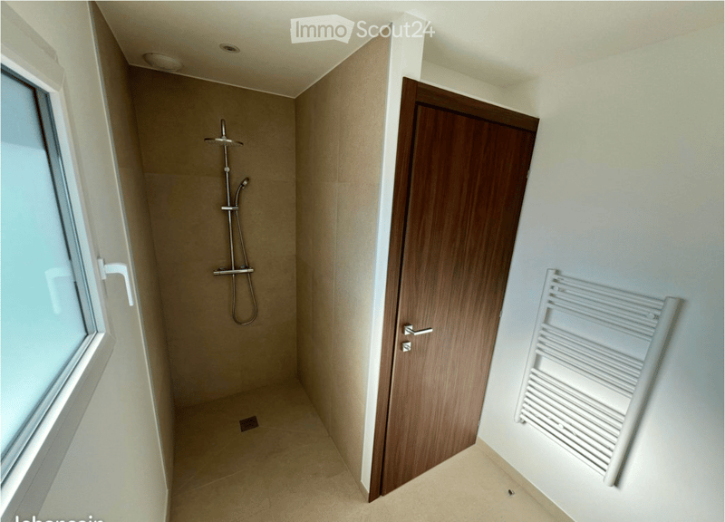 Modern bathroom with a shower area, a wooden door, a white radiator, and a window with frosted glass.