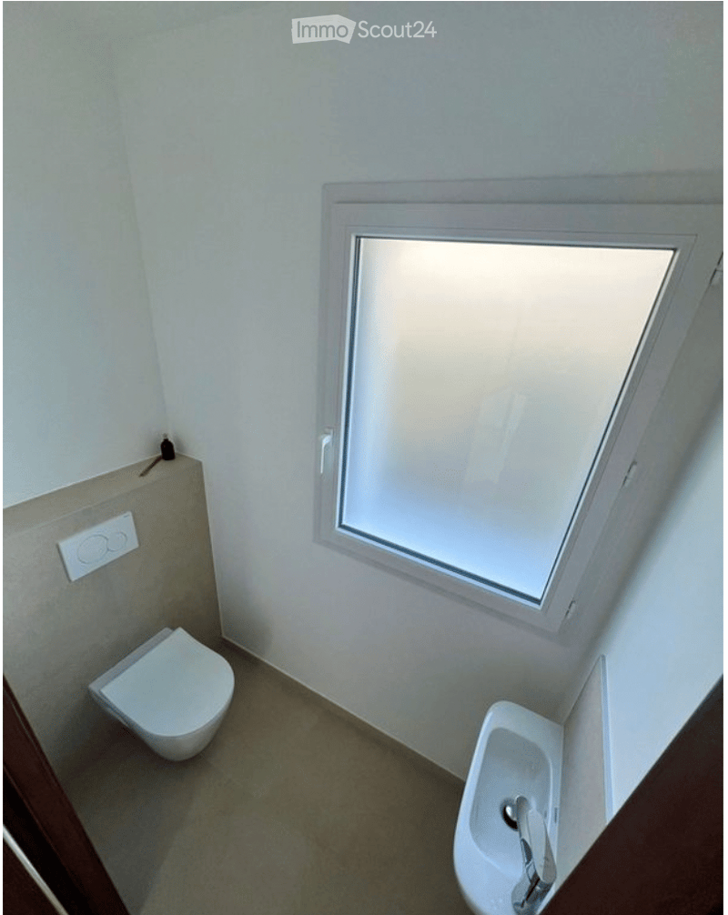 Compact bathroom with a toilet, bidet, and a small window for natural light. The walls are painted white, and the floor is tiled.
