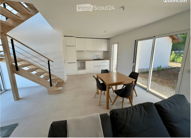 Open-plan living and dining area with a modern sofa, wooden dining table, chairs, and white kitchen cabinets.