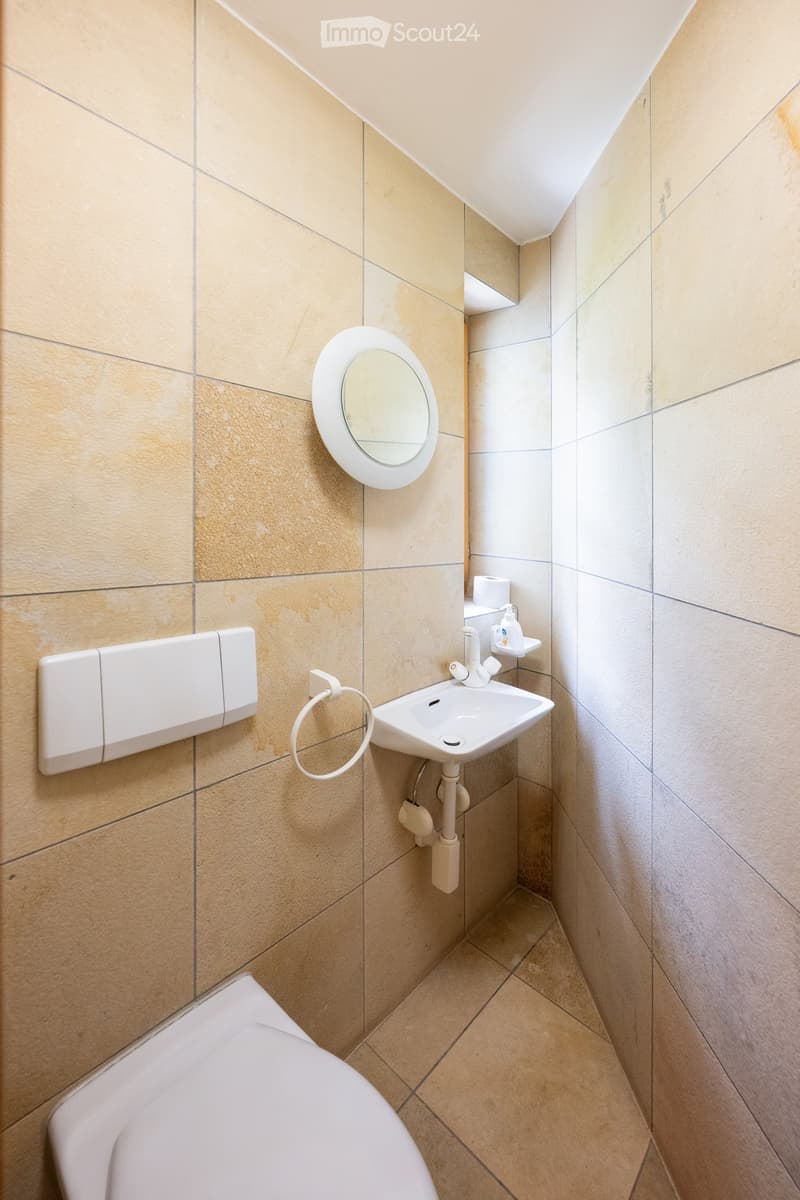 Compact bathroom with beige tiled walls and floor, featuring a toilet, sink with a mirror, and a soap dispenser.