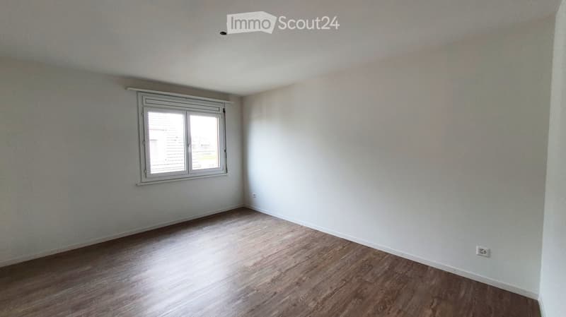Empty room with light-colored walls and wooden flooring, featuring a single window with blinds.
