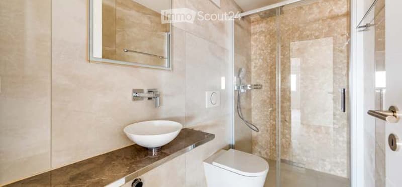 Modern bathroom with a white sink, mirror, toilet, and glass-enclosed shower. Light-colored tiles and sleek fixtures.