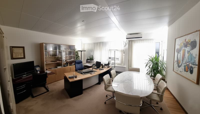 Office space with a large desk, multiple chairs, a round meeting table, a cabinet, and artwork on the walls.