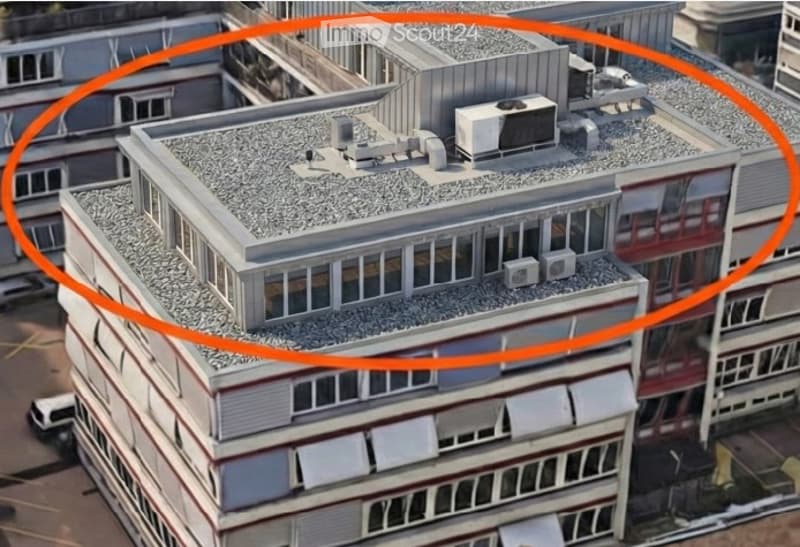 A multi-story building with a flat roof, visible air conditioning units, and surrounding structures.