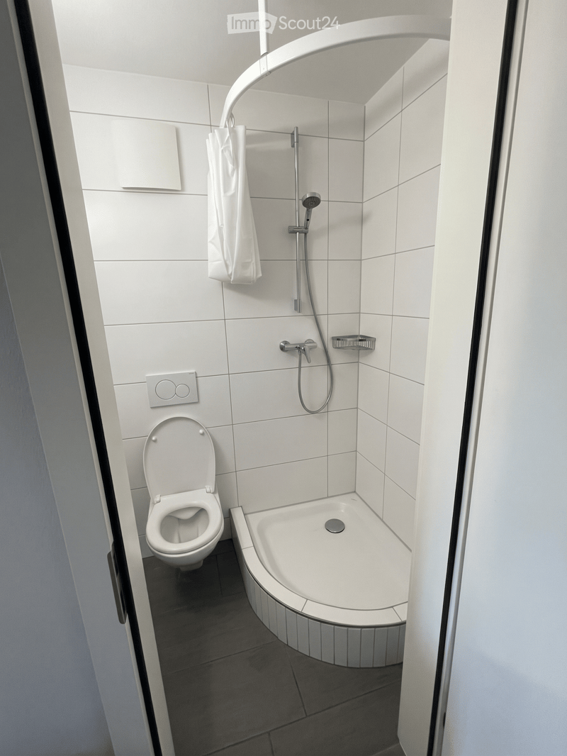 Modern bathroom with white tiles, a toilet, a bathtub, a showerhead, and a towel hanging on the wall.