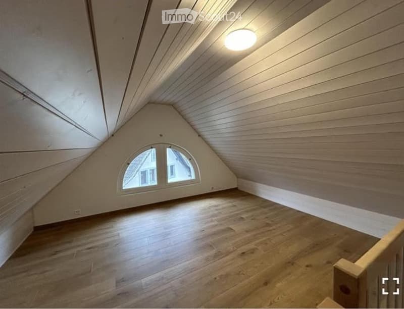 Empty attic room with wooden walls and floor, skylight window, and exposed wooden beams on the ceiling.