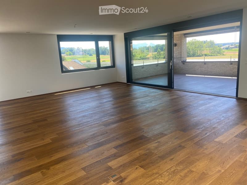 Empty room with wooden flooring, large windows, and sliding glass doors leading to a balcony or terrace.