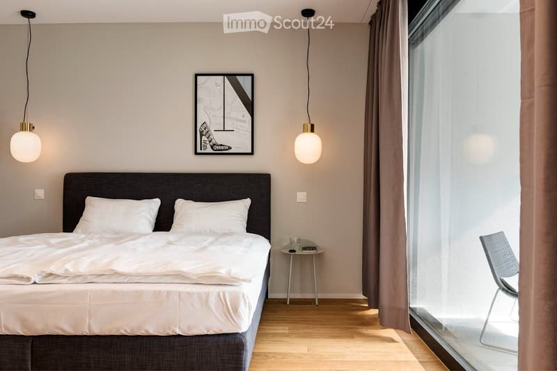 Modern bedroom with a large bed, nightstand, chair, pendant lights, and a picture frame on the wall.