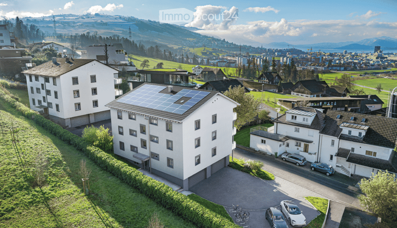 Aerial view of a residential area with multiple houses, solar panels on one roof, and parked cars in driveways.