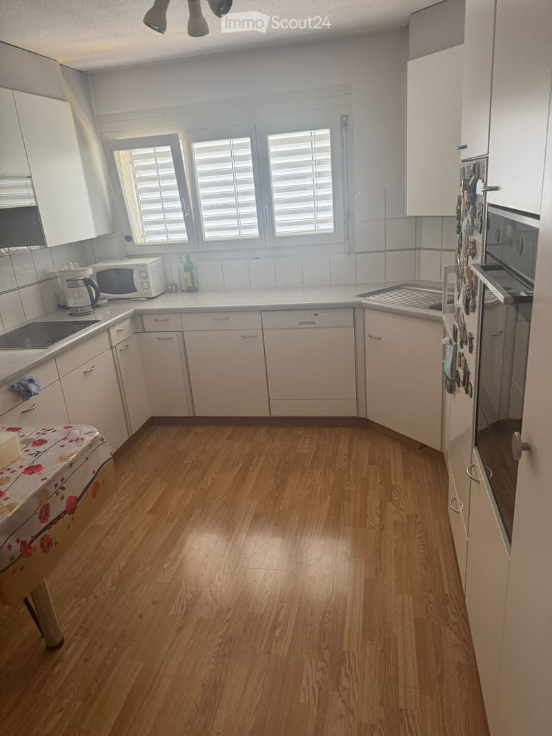 Modern kitchen with light-colored cabinets, wooden flooring, and stainless steel appliances including a microwave, electric kettle, refrigerator, oven, sink, and dishwasher.