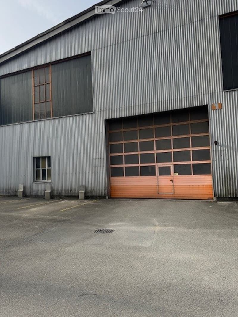 Industrial building with metal siding, large double garage door, windows, parking area