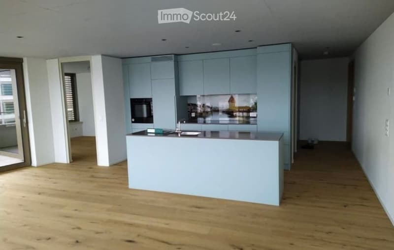 Modern kitchen with light blue cabinets, a central island, and a sleek design. The floor is made of light wood, and the space is bright and open.