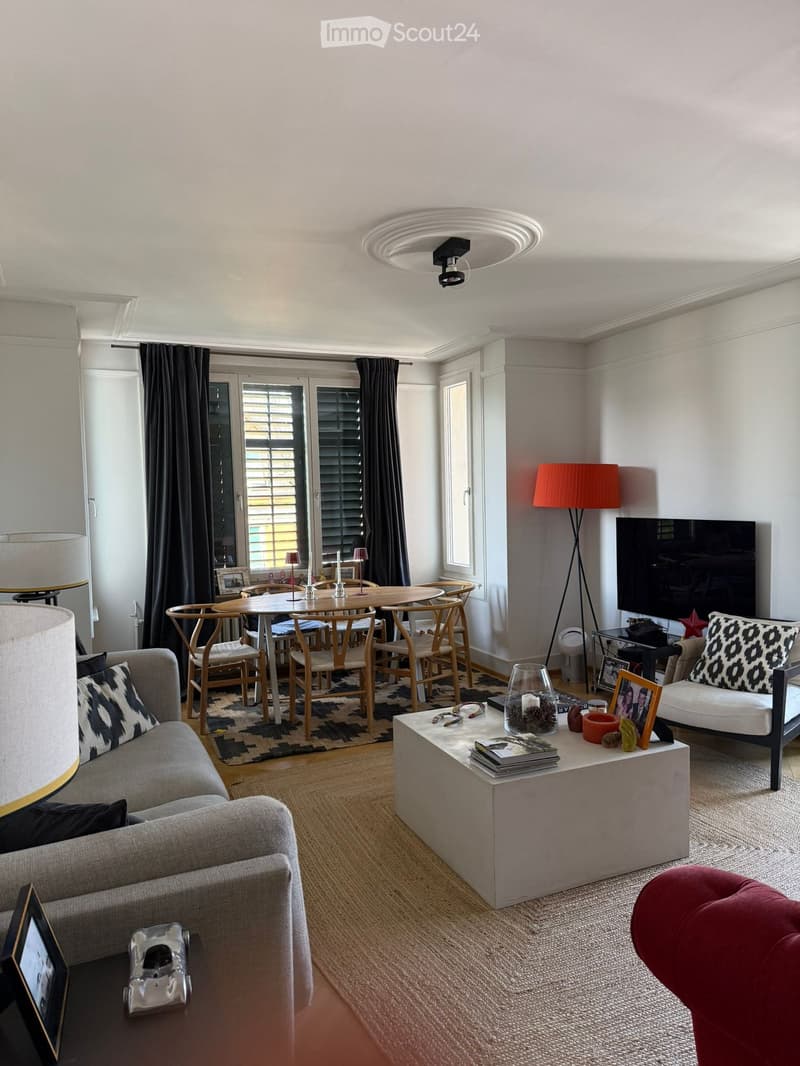 Modern living room with a grey sofa, coffee table, dining area with a round table and chairs, a large television, and decorative items on surfaces.