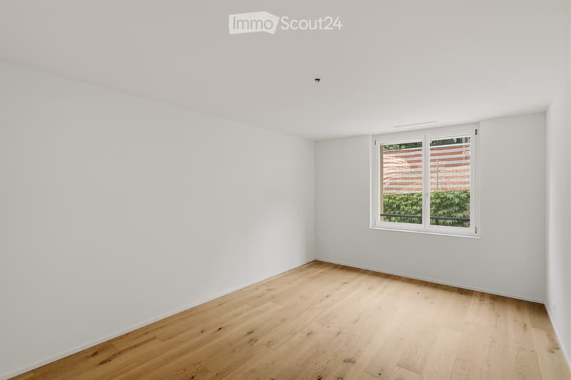 Empty room with white walls and light wooden flooring, featuring a single window with white frame and blinds.