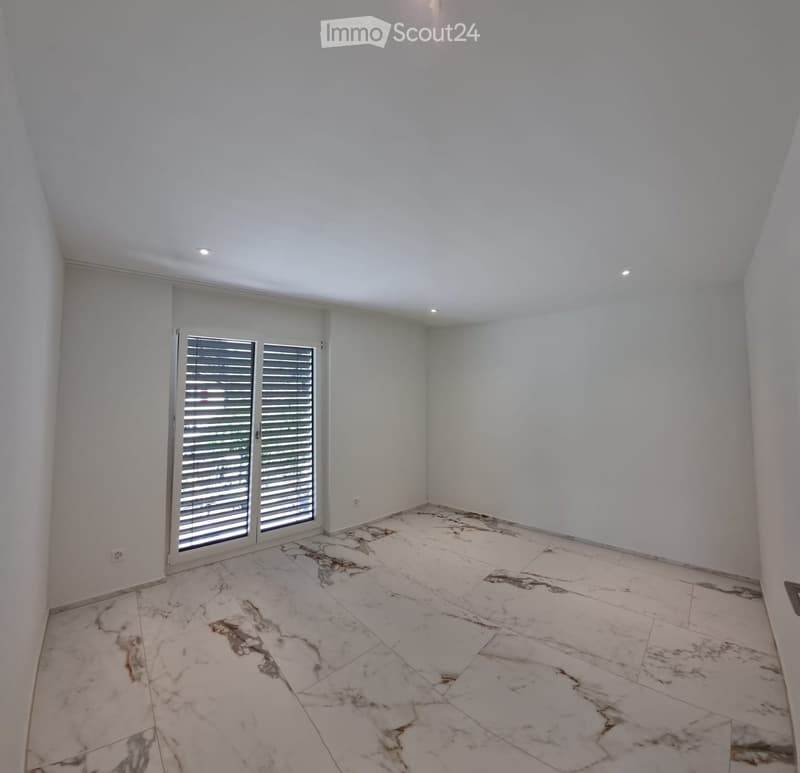 Empty room with white walls, marble flooring, and large sliding glass doors with blinds.