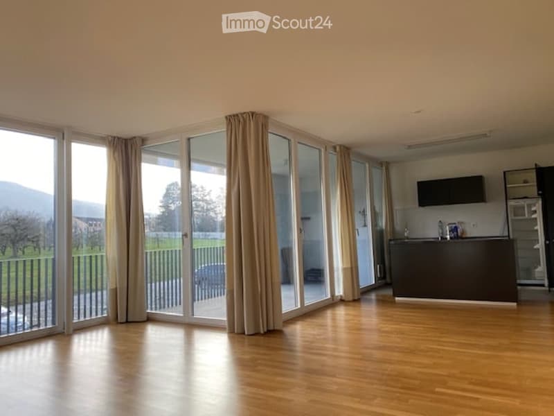 Open-plan living and kitchen area with wooden flooring, large glass sliding doors leading to a balcony with a scenic view, kitchen island, and modern appliances.