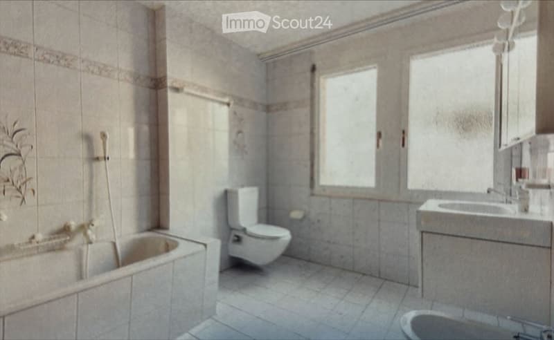 Bathroom with a bathtub, toilet, sink, and faucet. Light-colored tiles and a window provide natural light.