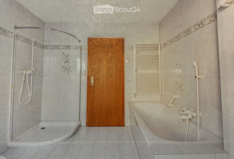 Modern bathroom with a glass-enclosed shower stall, a wooden door, and a radiator. The walls are tiled in a light grey color with decorative border tiles.