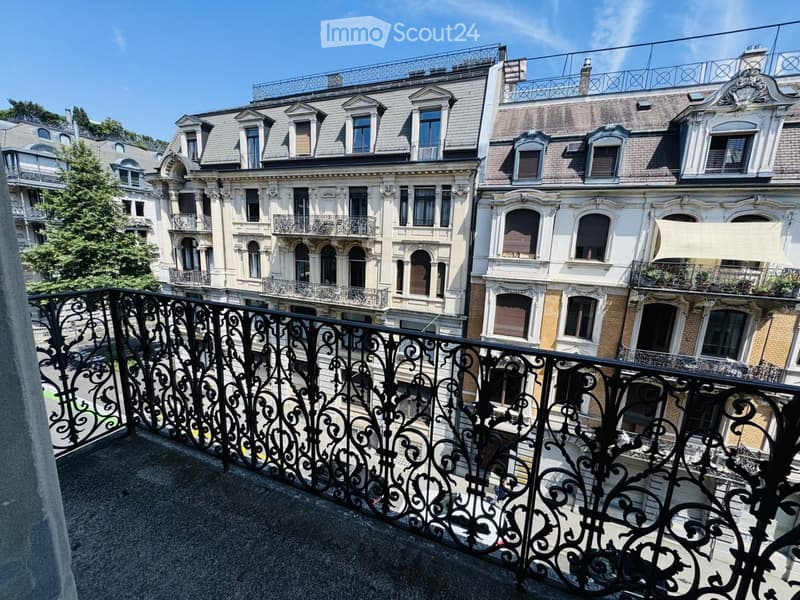Balcony with ornate black metal railing overlooking a street lined with historic buildings featuring ornate facades, multiple windows, and decorative elements.