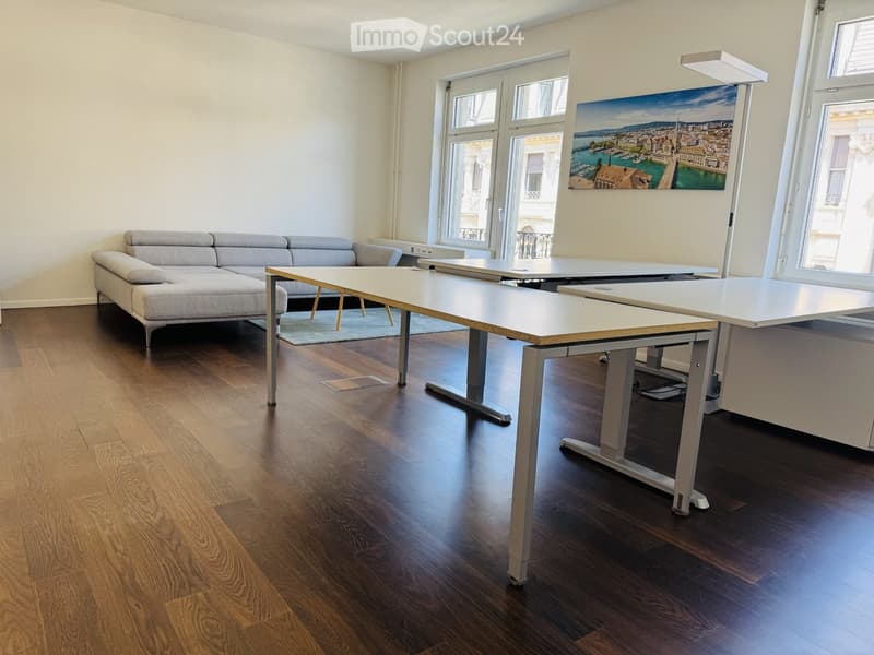 Modern living room with a grey sectional sofa, white tables, and large windows offering a scenic view.