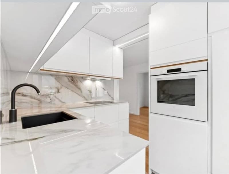Modern kitchen with white cabinets, marble countertops, a black faucet, and a built-in oven.